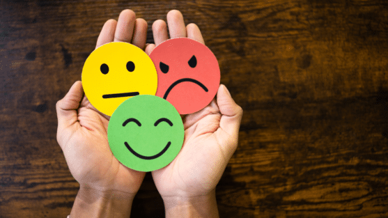 Three faces in hand - smiley face (green), neutral face (yellow) and angry face (red)